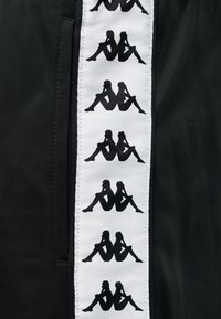 Μαύρη και άσπρη υφασμάτινη ταινία με επαναλαμβανόμενες μαύρες σιλουέτες ενός άντρα και μιας γυναίκας που κάθονται πλάτη με πλάτη σε μαύρα ρούχα.