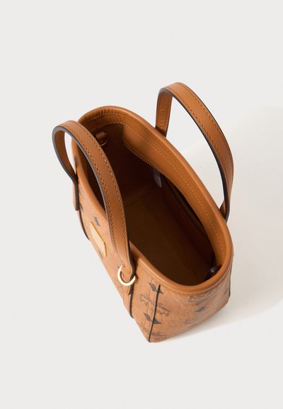 Petit sac à main en cuir beige avec deux anses, ouverture sur le dessus, détail anneau doré et logos noirs imprimés à l’extérieur.