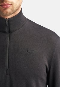 Mørkegrå højhalset pullover med en halv lynlås, lavet af ribbet stof, med et subtilt logo broderet på brystet.