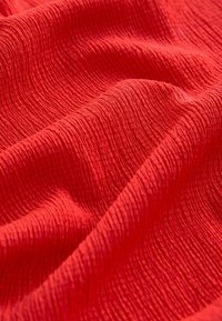 Tissu rouge avec une surface texturée et côtelée, et des plis doux créant de douces ondulations sur la matière.