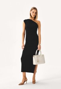 Fekete egyrészes ruha redős textúrával, világosszürke táskával és barna, hegyesorrú magassarkúval párosítva. Egyszerű, elegáns sziluett.