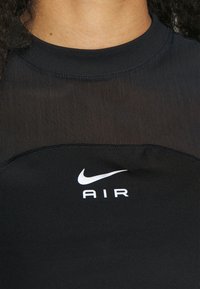 Camisa deportiva negra hecha de una tela suave y elástica. Presenta un cuello redondo y el logo blanco "Nike Air" en el pecho.