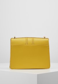 Gelbe strukturierte Handtasche mit einer strukturierten Oberfläche, ausgestattet mit einem goldenen Kettenriemen und einem schlichten, minimalistischen Design. Keine sichtbaren Logos oder Muster.
