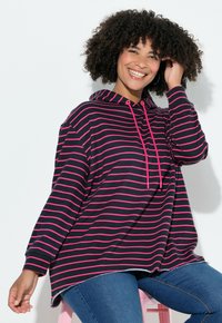 Gedurfde hoodie met marineblauwe en roze strepen, voorzien van een zak aan de voorkant, trekkoord aan de capuchon en een rafelige zoom. Gecombineerd met een blauwe spijkerbroek.