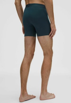 Sötét türkiz boxeralsó, rugalmas anyagból, szoros illeszkedéssel, látható minták nélkül és egyszerű gumipánttal.