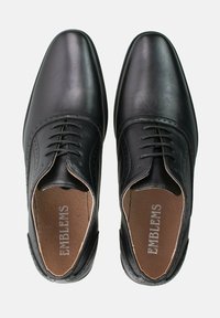 Zapatos de vestir de cuero negro con acabado pulido, diseño de cordones y detalles perforados decorativos a lo largo de los bordes.