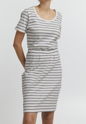 Vrouw draagt een witte jurk met korte mouwen en knielengte, met dunne horizontale zwarte strepen en een elastische taille.