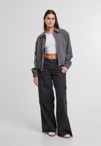 Gray zippered jacket with a collared neckline, paired with high-waisted black cargo pants featuring side pockets and frayed hems.