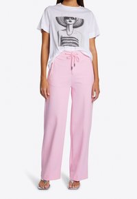 Witte T-shirt met een grafische afbeelding van een vrouw met een zonnebril, gecombineerd met losse roze broek met een trekkoord in de taille en zijzakken.