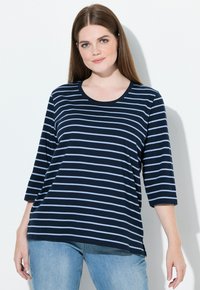 Laivastonsininen ja vaaleansininen raidallinen pitkähihaisella paidalla, jossa on pyöreä pääntie, rento istuvuus ja sivuaukot, yhdistettynä vaaleansinisiin farkkuihin.