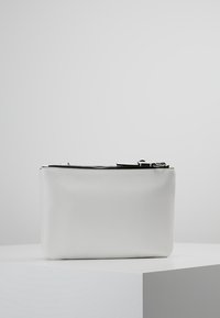 Biała skórzana torba w formie sakiewki o gładkiej fakturze, prostokątnym kształcie i srebrnym zamku błyskawicznym kontrastującym z górną krawędzią.