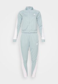 Survêtement Adidas bleu clair avec des bandes blanches sur les manches et le pantalon, veste avec fermeture éclair complète et pantalon fuselé avec taille élastique.