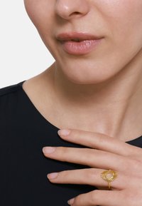 Goldringe mit Sonnenstrahlen-Design, mit einem zentralen Edelstein. Glatte Textur, kreisförmige Form. Am Finger gegen einen dunklen Oberteil getragen.