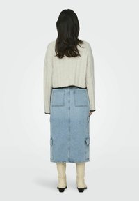 Cropped cream sweater with black trim paired with a blue denim midi skirt featuring cargo pockets, complemented by knee-high tan boots.
