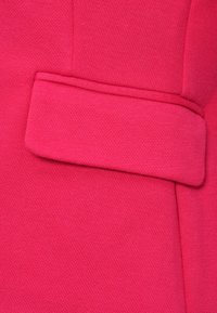 Gros plan d’un tissu rose vif avec un détail de rabat horizontal cousu sur une surface texturée.
