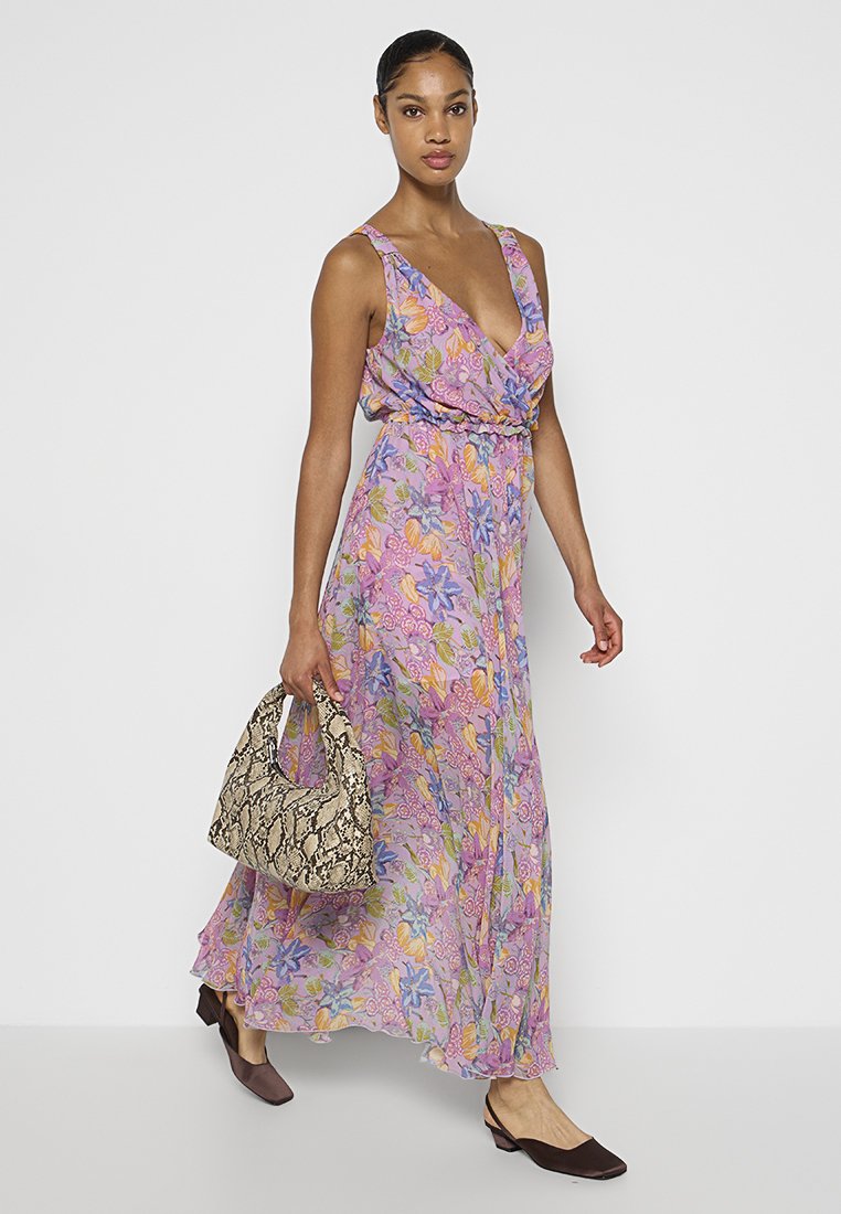 Fioletowa maksidiania sukienka z głębokim dekoltem w kształcie V i zwiewnym kroju, uzupełniona beżową torebką w wężowy wzór i brązowymi butami wsuwanymi.