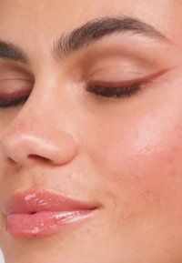 Lähikuva kasvoista, joissa on sileä iho, luonnollinen ihonsävy, pehmeän vaaleanpunaiset kiiltävät huulet ja hillitty silmämeikki.
