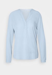 Chemise bleu clair à manches longues en tissu doux, avec une patte boutonnée et un ourlet légèrement arrondi. Design minimaliste sans motifs.