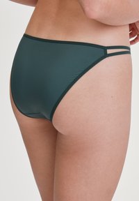 Dunkelgrüner Bikini-Unterteil aus glattem Stoff. Bietet minimalen Schnitt mit dünnen Seitenträgern. Die Textur wirkt weich und dehnbar.