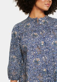 Blå blus med paisleymönster och mandarinkrage, knappstängning och samlade ärmar. Tyget har en mjuk textur med intrikata mönster.