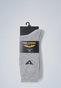 Calze in cotone grigio mescolato esposte con un'etichetta nera caratterizzata da testo dorato e un logo, che mostrano un design semplice e funzionale.