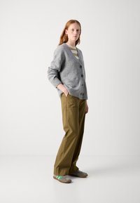 Gray wool cardigan with buttons, paired with olive green trousers. Model wears a striped shirt underneath and gray shoes with green accents.