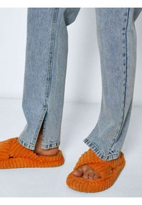 Chinelos laranja texturizados com um padrão estriado, combinados com jeans de denim azul claro com rachas laterais na barra.