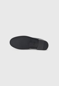 Talpa neagră din cauciuc a unei încălțăminte, având o suprafață netedă cu o textură ușoară și detalii de cusătură. Design minimalist, fără logo-uri vizibile.
