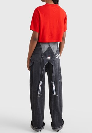 Red cropped cotton t-shirt paired with dark gray denim overalls featuring large front pockets, zippers, and logo detailing.