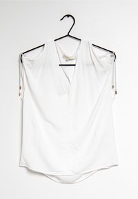 White, short-sleeved blouse with a deep V-neck and rounded hem, made from smooth fabric. Features drawstring accents at the shoulders.