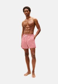 Bañadores rojos de estampado con cintura ajustable, bolsillos laterales y corte relajado, exhibidos en un modelo.
