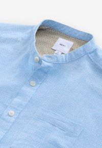 Hele sinine nööbitav särk, millel on tekstureeritud kangas, mandarinkaelus, eesmine tasku ja mustriline sisemine vooder. Kaubamärgi silt: NEXT.