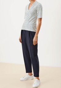 Camisa de cuello en V a rayas en blanco y azul marino, de mangas cortas, combinada con pantalones azul marino y zapatillas blancas, mostrando un ajuste relajado.