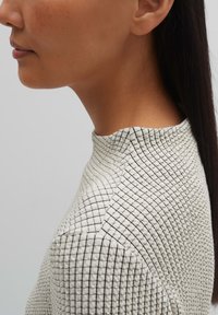 Strukturierter, leichter Pullover in Weiß mit einem schwarzen Karomuster. Mit einem hohen Kragen und einer taillierten Silhouette, die das Seitenprofil zeigt.
