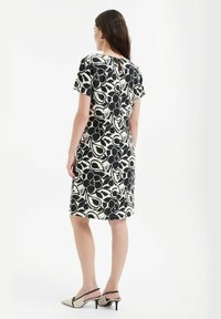 Sukienka z krótkim rękawem w czarno-białym kwiatowym wzorze, do kolan, z detalem w kształcie klucza z tyłu. Połączona z beżowymi obcasami z czarnymi akcentami.