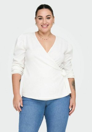Weiße Wickelbluse mit langen Puffärmeln, strukturiertem Stoff und seitlichem Bindeband. Kombiniert mit blauen Jeans.