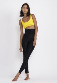 Yellow crop top paired with high-waisted black leggings featuring a ruched design. Smooth fabric, fitted style, minimal seams, and no visible patterns.