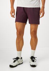 Bordeaux trenirke s glatkom završnom obradom, s malom logotip oznakom. Nošene uz bijele čarape do članaka i sportske cipele.