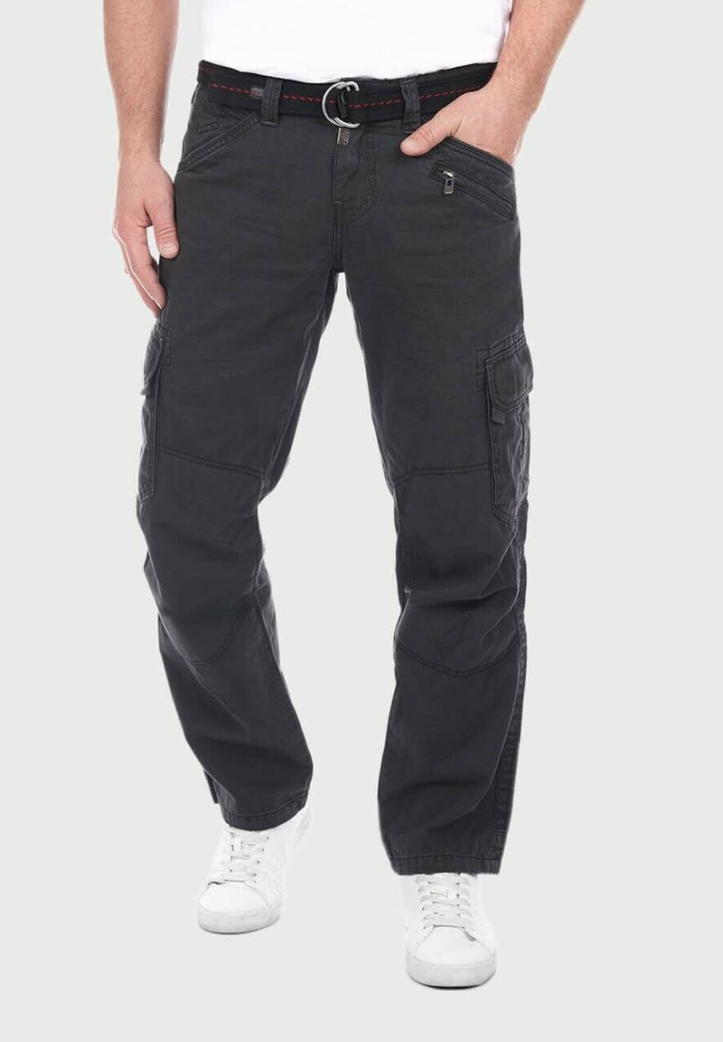 Schwarze Cargo-Hosen aus strapazierfähigem Material, mit mehreren Taschen, einer Reißverschlusstasche und einem rot akzentuierten Gürtel mit einer Metallschnalle. Weiße Sneaker.