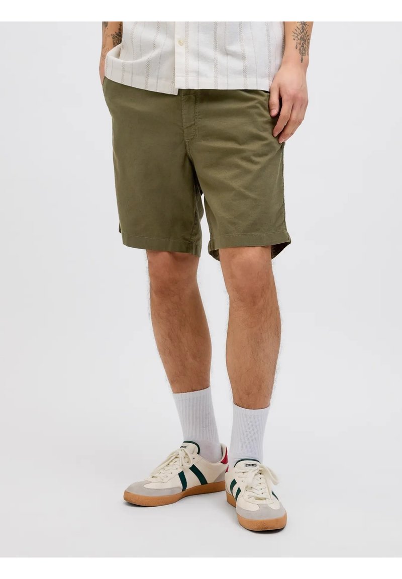 Shorts de algodón verde oliva con corte recto, que presentan bolsillos frontales y un dobladillo enrollado, combinados con calcetines blancos y zapatillas.