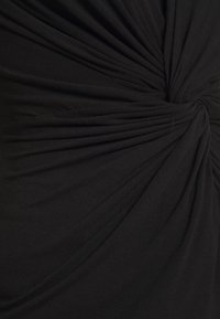 Svart tyg vridet i en samlad knut som skapar strålande veck och textur på ett mjukt, elastiskt material.