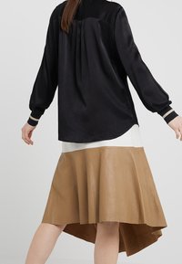 Schwarze Seidenbluse mit voluminösen Ärmeln und gestreiften Manschetten, kombiniert mit einem fließenden, hellbraunen Lederrock mit asymmetrischem Saum.