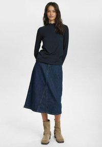 Långärmad svart topp med volangutskärning, ihop med en knälång blå denimkjol och beiga ankelstövlar med spänndetalj.