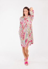 Abito rosa a maniche lunghe con motivo paisley blu e oro; in tessuto leggero; presenta un colletto e tasche laterali. Indossato con sandali rosa.