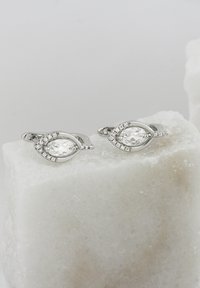 Silverörhängen med en oval klar ädelsten, omgiven av mindre stenar, med ett bladliknande mönster och slät yta.