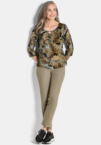 Multikleurige top met bloemenpatroon en 3/4-mouwen, gecombineerd met licht kaki pantalons en zwarte sneakers, met een ronde hals en knoopdetails.
