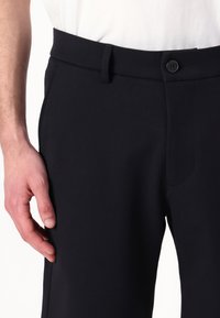 Black tailored trousers featuring a smooth texture, flat front, side pockets, and a button closure at the waistband.