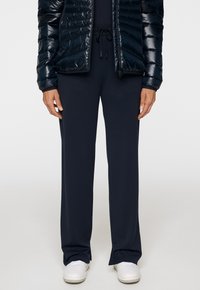 Niebieskie spodnie z szerokimi nogawkami wykonane z gładkiego materiału, z elastycznym pasem i sznurkiem, w połączeniu z ciemną puchową kurtką i białymi butami.