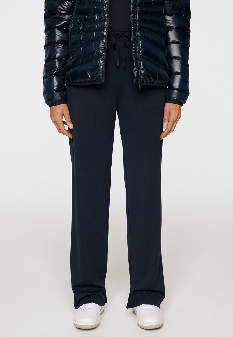 Niebieskie spodnie z szerokimi nogawkami wykonane z gładkiego materiału, z elastycznym pasem i sznurkiem, w połączeniu z ciemną puchową kurtką i białymi butami.