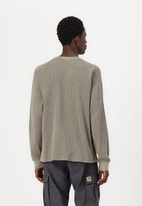 Langärmliges, hellgraues Strickshirt mit strukturiertem Muster und Raglanärmeln. Entworfen mit einem runden Halsausschnitt und enganliegenden Bündchen.